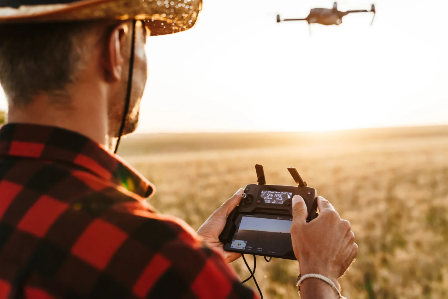 Image from back of focused man in straw hat using drone while standing at cereal field